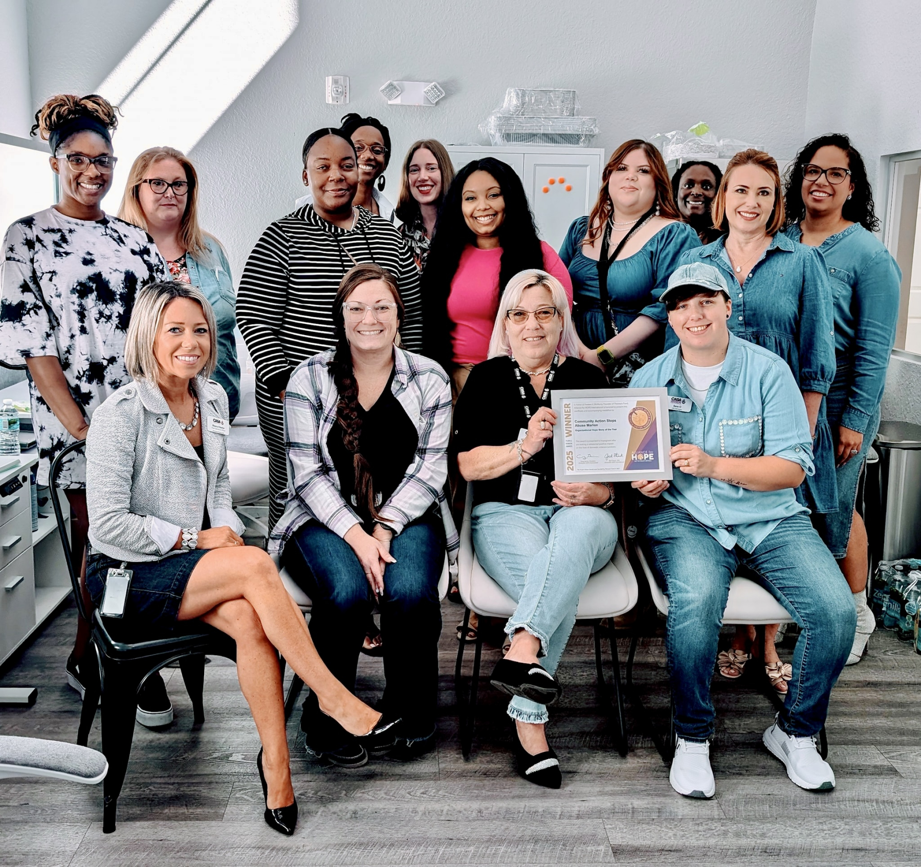A team of smiling professionals proudly holds a Purple Ribbon Award from DomesticShelters.org, celebrating their achievement in a bright, welcoming office space.