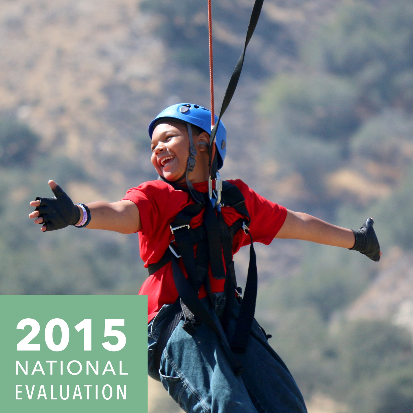 Camper on a zip line with his arms open and a wide smile as he looks behind him