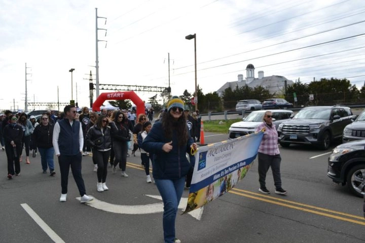 person giving thumbs up while walking with a banner at Walk a Mile in Her Shoes event