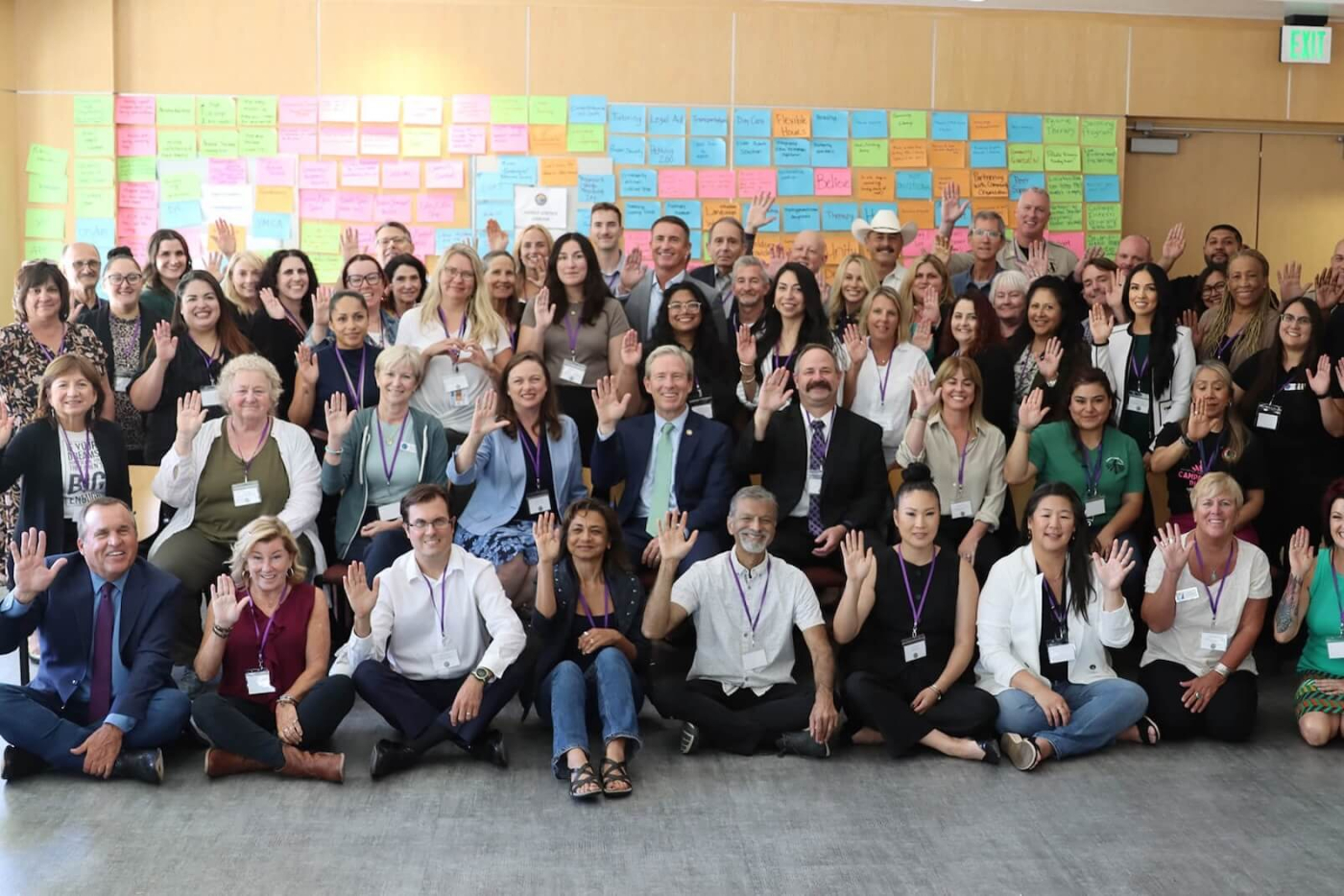 A large group of people gathered together for an FJCA related event with colorful sticky notes in the background